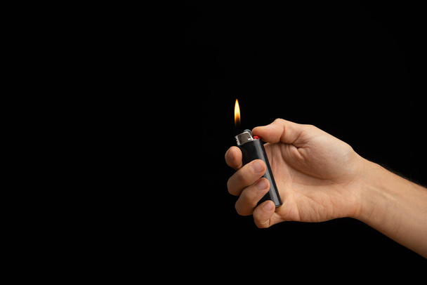 mano de un hombre que entrega un encendedor encendido sobre un fondo negro liso que viene del lado derecho - Foto, imagen