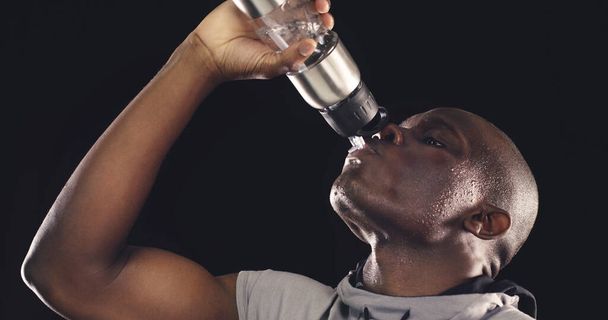 Apagando mi sed antes de hacer mis últimas repeticiones. Estudio de un joven deportista bebiendo de una botella de agua sobre un fondo oscuro. - Foto, Imagen