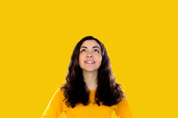 Brunette pensive girl looking up on a yellow background - Photo, Image