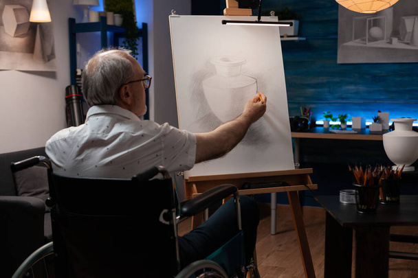 Senior uomo artista utilizzando sedia a rotelle disegno originale disegno a matita di natura morta vaso sensazione creativa su cavalletto - Foto, immagini