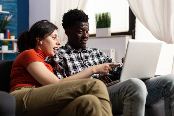Fröhliches junges multiethnisches Paar blickt auf Computerbildschirm - Foto, Bild