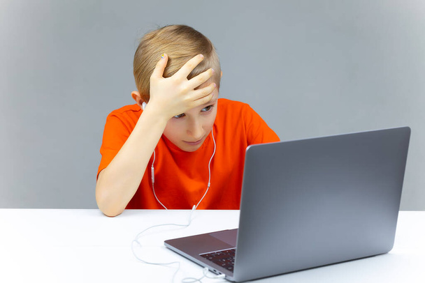 Ένα αγόρι με ένα φορητό υπολογιστή για online εκπαίδευση άρπαξε το κεφάλι του - Φωτογραφία, εικόνα