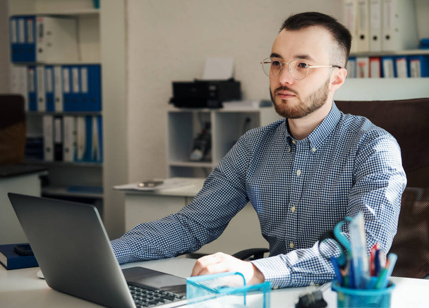 Jovem empresário de camisa trabalhando em seu laptop em um escritório - Foto, Imagem