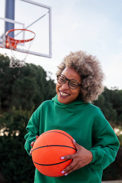 young latin woman laughing on a basketball court with a ball in his hands, concept of urban sport in the street, copy space for text - Foto, Imagen