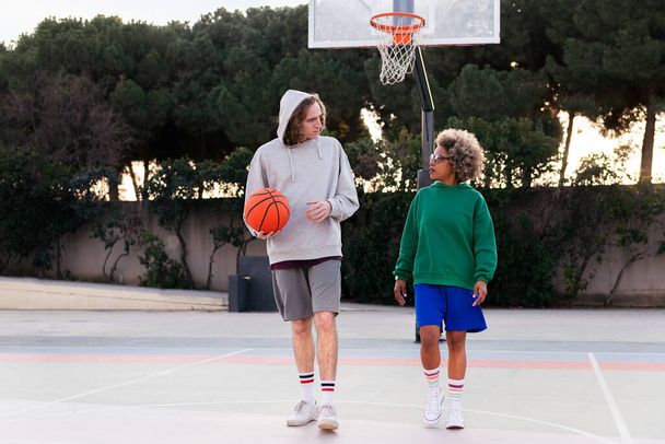 latin woman and caucasian man chatting while walking on the basketball court after a game, concept of friendship and urban sport in the street, copy space for text - Fotó, kép