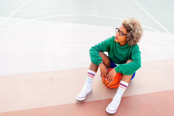 latin woman resting while sitting on the court after basketball practice, concept of urban sport outdoors, copy space for text - Foto, immagini