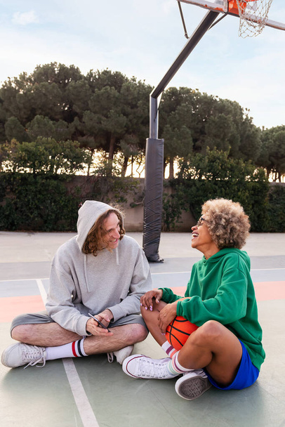 man and woman laughing and having fun with the phone after basketball practice in a city park, concept of friendship and urban sport in the street, copy space for text - Photo, image