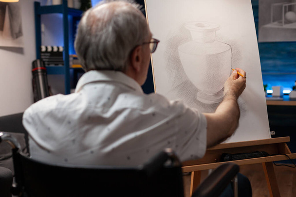 Detailní portrét staršího muže umělec pomocí invalidního vozíku kreslení originální tužkou kresba vázy na stojanu - Fotografie, Obrázek