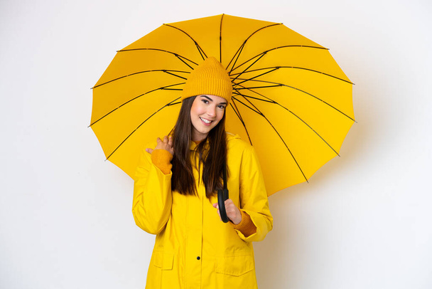 Young Brazilian woman with rainproof coat and umbrella isolated on white background laughing - Foto, Imagem