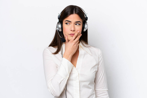 Telemarketer běloška pracující se sluchátky izolované na bílém pozadí s pochybnostmi a s zmateným výrazem ve tváři - Fotografie, Obrázek