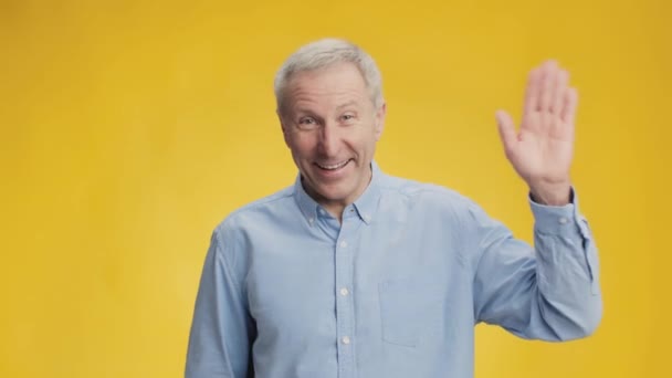¿Hola? Feliz hombre mayor sociable emocionado saludando de la mano a la cámara y sonriendo, saludando alegremente, fondo amarillo - Imágenes, Vídeo