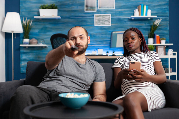 Casal adulto multiétnico sentado no sofá e assistindo programas de televisão - Foto, Imagem