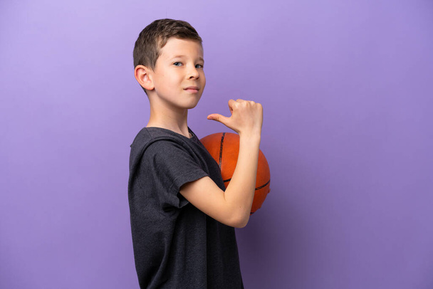 Malý chlapec hraje basketbal izolované na purpurovém pozadí hrdý a self-spokojen - Fotografie, Obrázek