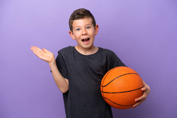 Niño jugando baloncesto aislado sobre fondo púrpura con expresión facial impactada - Foto, imagen