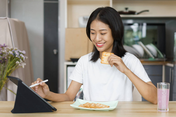 Otthon életmód koncepció, fiatal nő használja tabletta és étkezési keksz, míg a szabadidő otthon. - Fotó, kép
