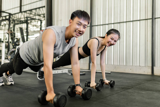 exercise concept The female and male members of the gym doing the basic renegade row posture with dumbbells while looing at each other face. - Photo, Image