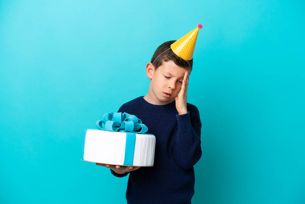Little boy holding birthday cake isolated on blue background with headache - 写真・画像