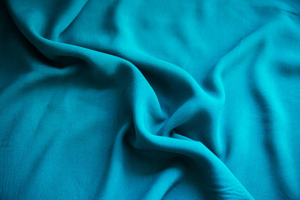 Tejido arrugado azul se encuentra en pliegues sobre la mesa con cortinas. - Foto, Imagen