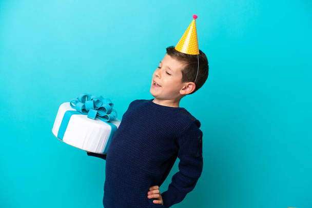 Malý chlapec drží narozeninový dort izolované na modrém pozadí trpí bolestí zad za to, že vynaložil úsilí - Fotografie, Obrázek