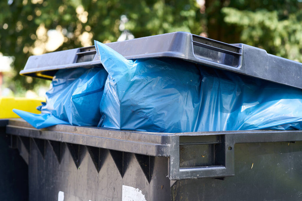 A full dumpster with garbage bags sticking out. The garbage disposal has to pick up the container.                            - Photo, Image