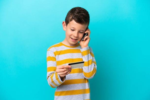 Kisfiú elszigetelt kék háttér vásárol a mobil egy hitelkártya - Fotó, kép