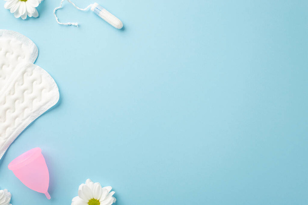 Horní pohled fotografie heřmánku květinové pupeny hygienické ubrousky růžové menstruační pohár a tampón na izolované pastelové modré pozadí s copyspace - Fotografie, Obrázek