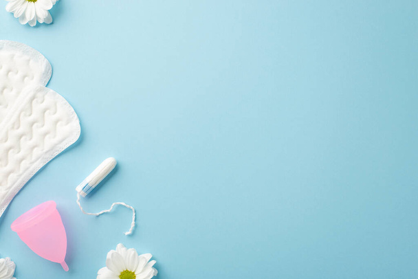 Bovenaanzicht foto van kamille bloemknoppen hygiënische pads roze menstruatiecup en tampon op geïsoleerde pastelblauwe achtergrond met copyspace - Foto, afbeelding