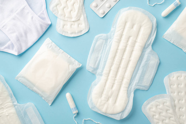 Top view photo of hygienic pads tampons panties and painkiller pills on isolated pastel blue background - Фото, зображення
