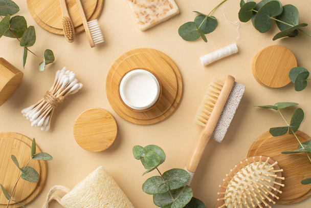 Eco cosmetics concept. Top view photo of bamboo foot brush and pumice cream jar soap dental floss toothbrushes hair brush cotton buds green plant leaves and wooden stands on isolated beige background - Photo, Image