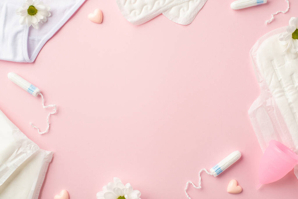 Top view photo of camomile flower buds small hearts lingerie menstrual cup sanitary napkins and tampons on isolated pastel pink background with copyspace in the middle - Φωτογραφία, εικόνα