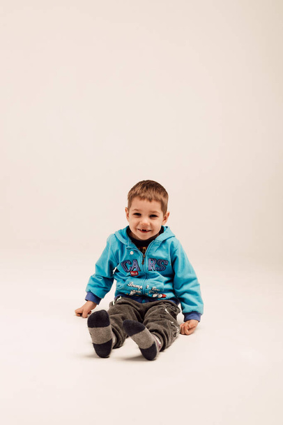 A little boy in a blue jacket sits on a white background - 写真・画像