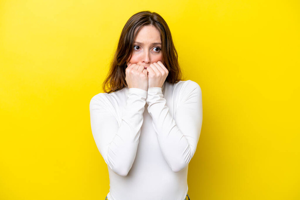 Young caucasian woman isolated on yellow background nervous and scared putting hands to mouth - Foto, immagini