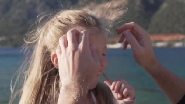 Close-up, slow-motion shooting, a mans hand removes disheveled hair from the face of a little girl against the background of the sea - Footage, Video