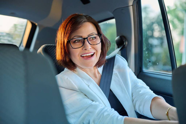 Портрет элегантной женщины среднего возраста в машине на заднем пассажирском сидении - Фото, изображение