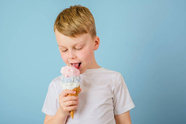 Positiver Junge leckt Eis auf blauem Hintergrund. Gesundheit profitiert Eiscreme-Konzept. Hochwertiges Foto - Foto, Bild