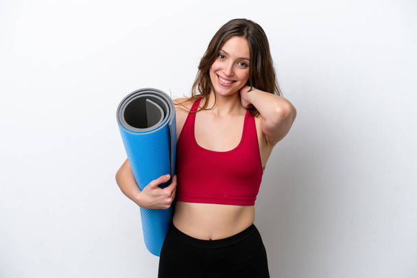 Young sport caucasian woman going to yoga classes while holding a mat isolated on white background laughing - Photo, image