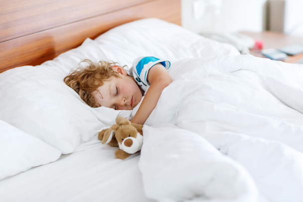 Adorable kid boy sleeping and dreaming in his white bed with toy - Fotó, kép