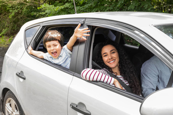 Glad young arabic man and woman driving car, little excited boy with open mouth gesturing, waving with hands at window - Foto, imagen