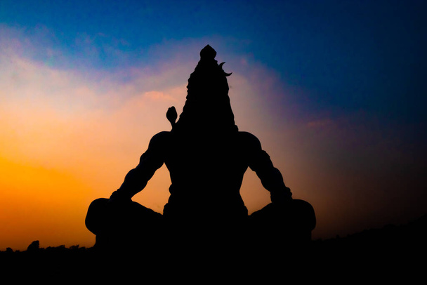 terug verlicht standbeeld van hindoe god heer shiva in meditatie houding met dramatische lucht van unieke hoek afbeelding wordt op parmarth niketan rishikesh uttrakhand india genomen. - Foto, afbeelding