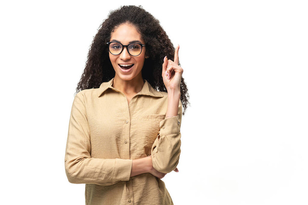 Happy young multiracial curly smiling woman 20s holding index finger up in sign of great solution - 写真・画像