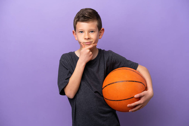 Mały chłopiec gra w koszykówkę odizolowany na fioletowym tle myślenia - Zdjęcie, obraz