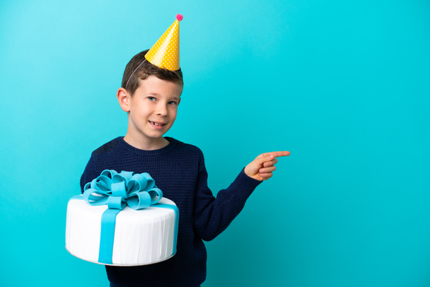 小さな男の子保持誕生日ケーキの側に指を指す青の背景に隔離 - 写真・画像