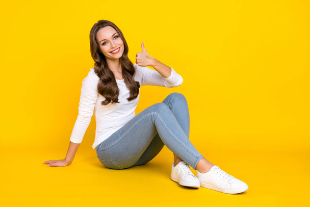 Photo of charming sweet lady dressed white shirt sitting floor showing thumb up isolated yellow color background - 写真・画像