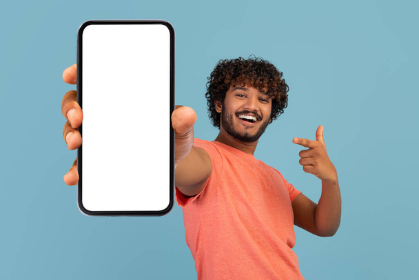 Cool curly indian guy showing cell phone with empty screen - Fotó, kép
