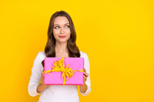 Photo of sweet thoughtful lady dressed white shirt holding gift looking empty space isolated yellow color background - 写真・画像