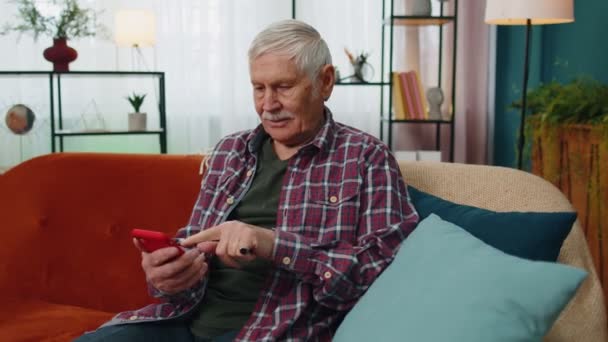 Overjoyed idős nagyapa férfi hold smartphone, izgatott a mobil app sport fogadás nyeremény otthon - Felvétel, videó