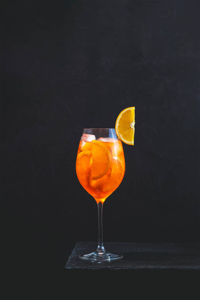 Koktajl Aperol Spritz w wielkim kieliszku do wina z kropli wody na ciemnym tle. Letni koktajl alkoholowy z pomarańczowymi plasterkami. Włoski koktajl Aperol Spritz na pokładzie łupków. Modny napój - Zdjęcie, obraz