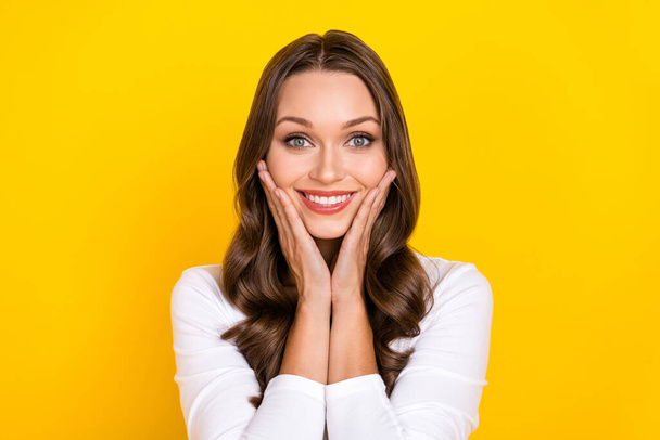 Photo of cheerful glad pretty adorable lady palms cheeks shiny smile wear white shirt isolated yellow color background - Φωτογραφία, εικόνα