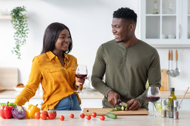 Kocası mutfakta salata pişirirken Mutlu Siyah Kadın Şarap İçiyor - Fotoğraf, Görsel