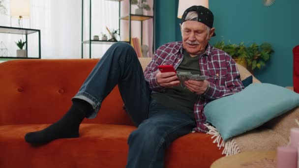 Lächelnder älterer Mann mit Bargeld und Smartphone, zufrieden mit dem Einkommen, Familienbudget planen - Filmmaterial, Video